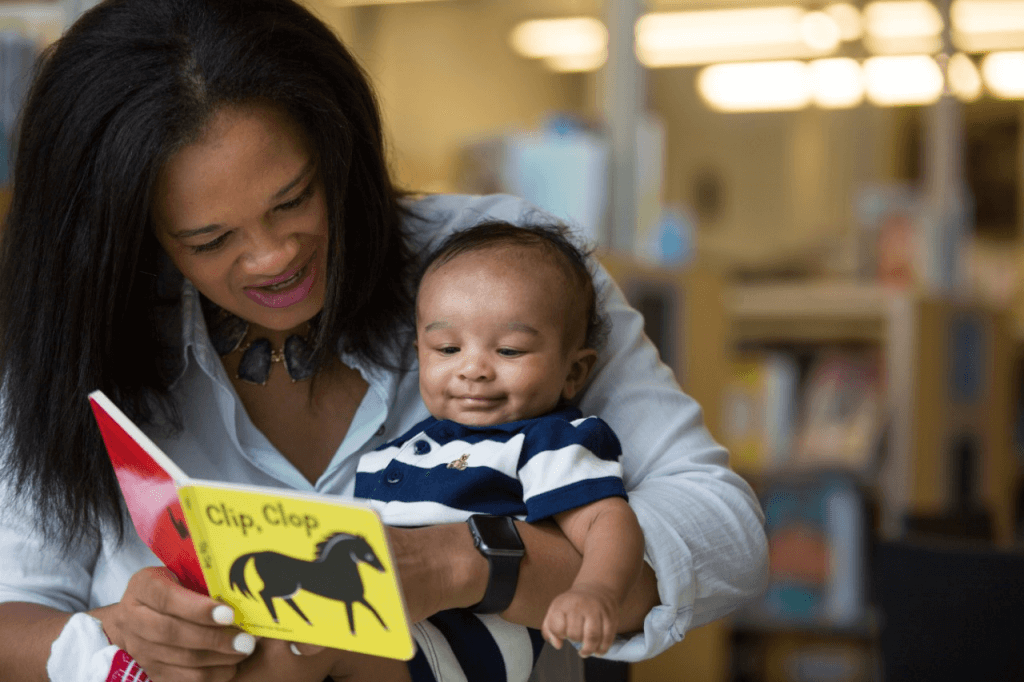 A smiling baby and caregiver read the book, Clip Clop.