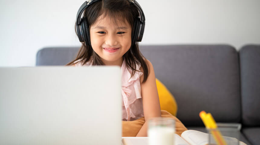 Young child wearing headphones smiles at her computer during virtual learning