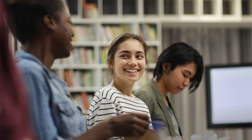 Three teens smiling and talking in the library.