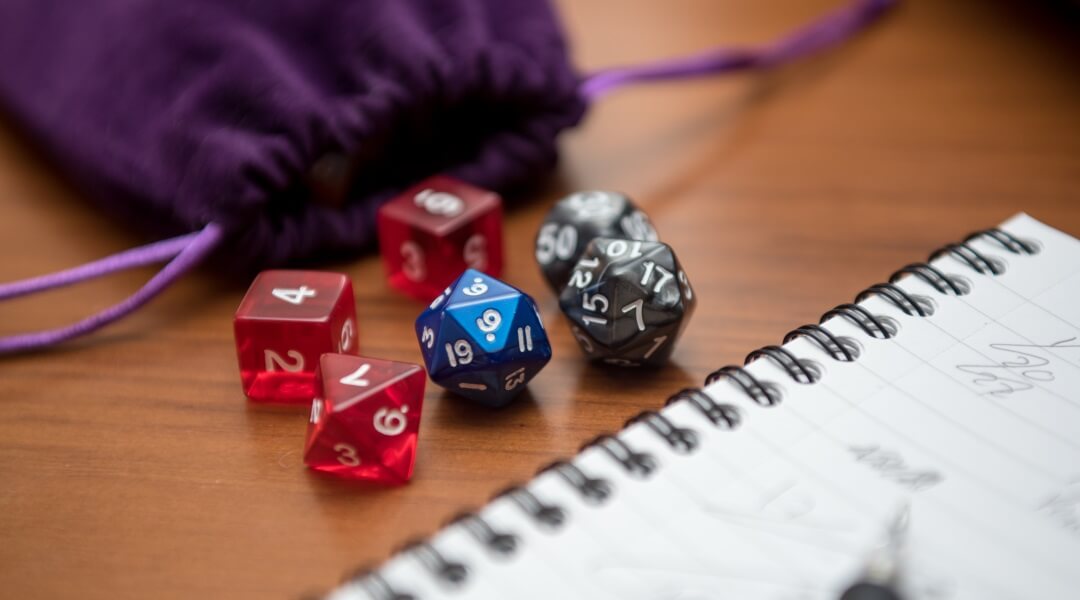 A set of dice sitting on a table next to a purple velvet sack and notebook.