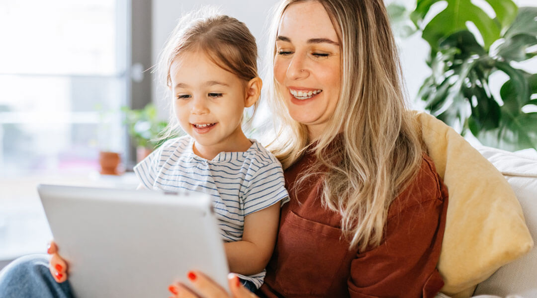 A smiling adult and young child watch a tablet together.