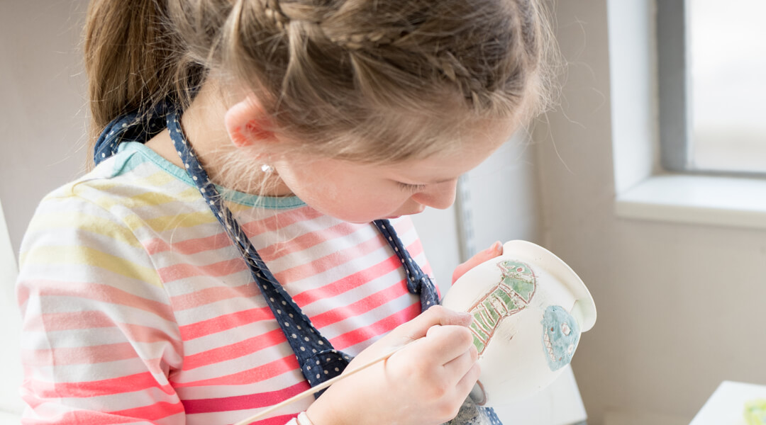 A child paints dinosaurs on a clay pot