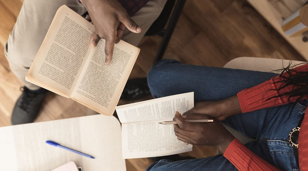 Birds eye view of two adults sitting in the library, reading and analyzing a novel together