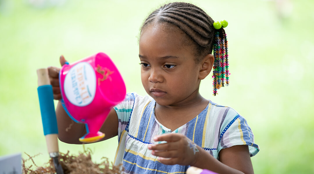 A young child pretends to water flowers with a toy watering can.