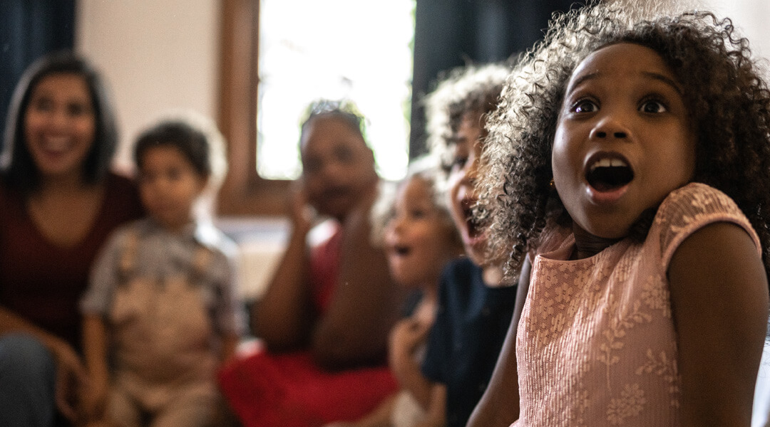 A child reacts with awe while watching a movie with others.