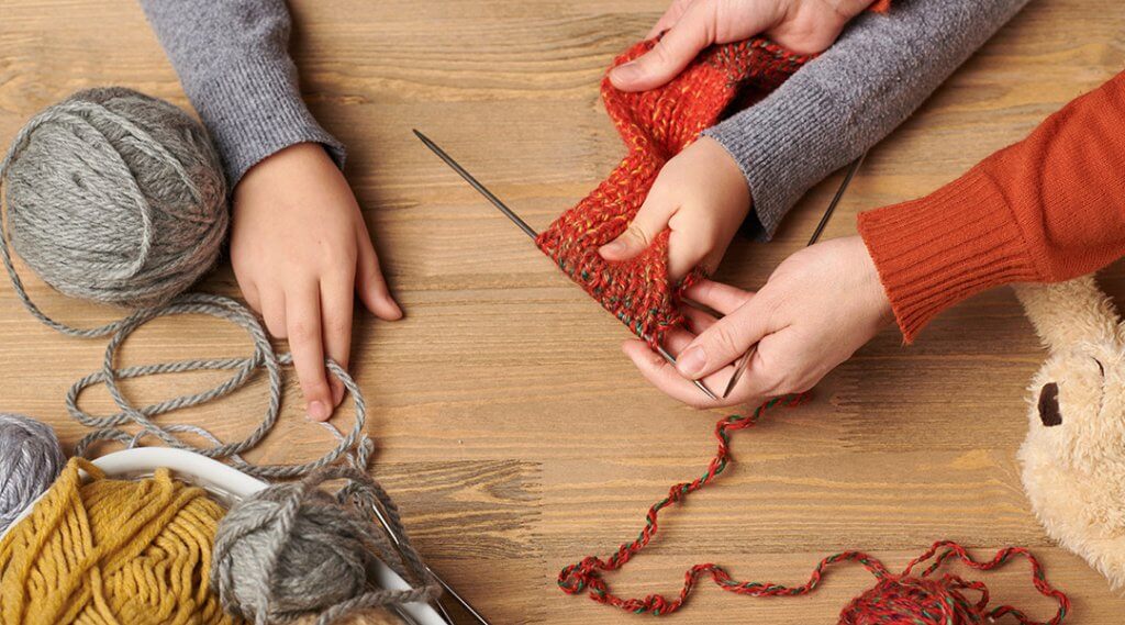 Close up of adult and child's hands as the child learns to knit.