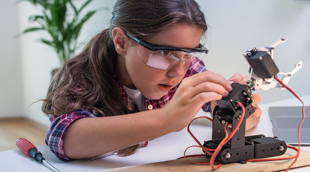 A tween closely inspects wires on a small robotic object.