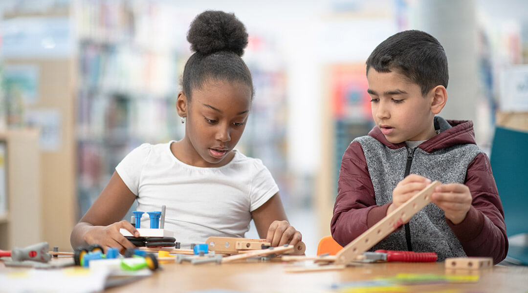 Two elementary school age children are building a project together at their public library.