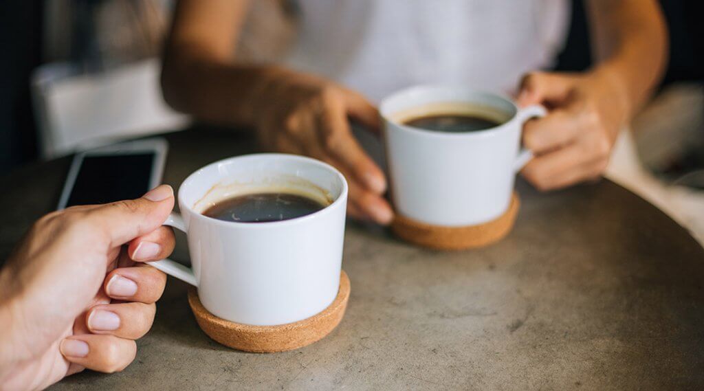 Close up of two people holding cups of coffee at a small cafe table.