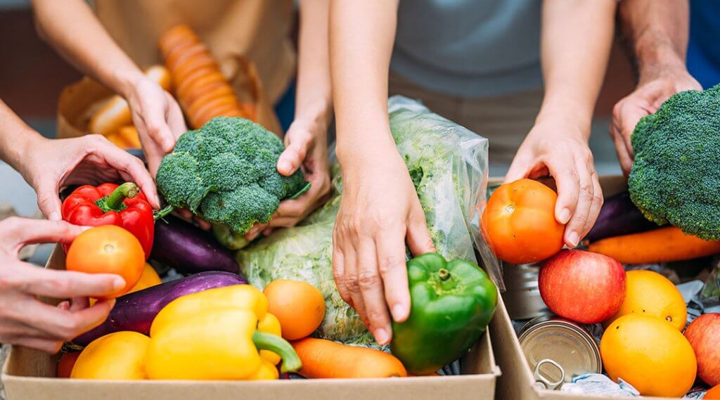 Volunteers hands collecting grocery products, foodstuff to food donations box.