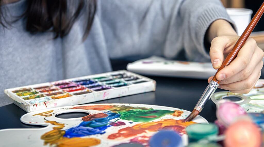 A young woman draws with paints with a brush, close-up.