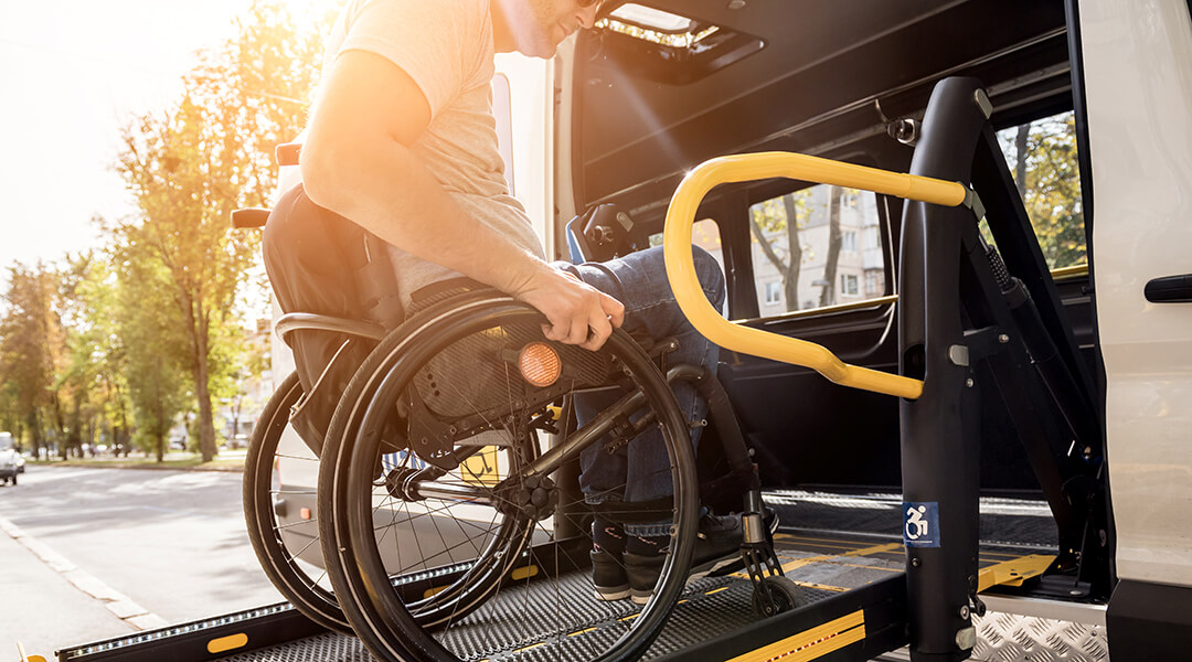 An adult in a wheelchair on a lift of a vehicle for people with disabilities.