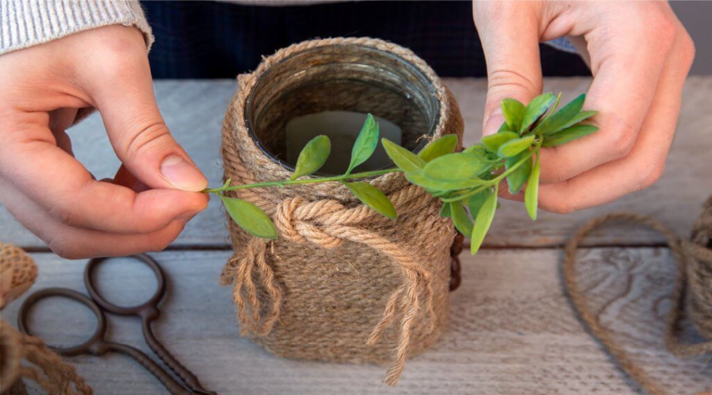 Close-up of hands tying twine and decorative leaves around a tin can.