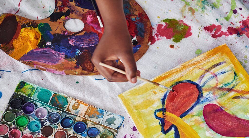 Overhead view of a hand painting a piece of paper on a messy drop-cloth.