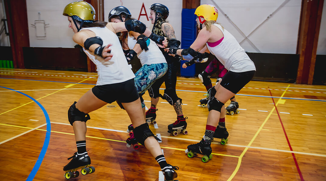 Four people wearing roller skates and protective gear vie to race ahead of one another.