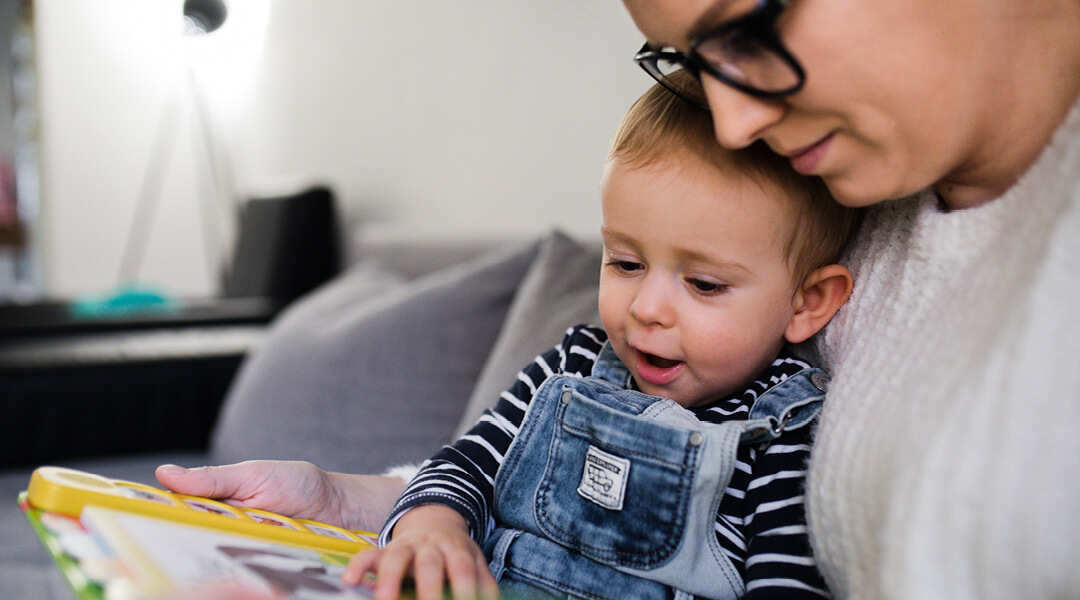 Adult cuddling with a toddler reading a book together.