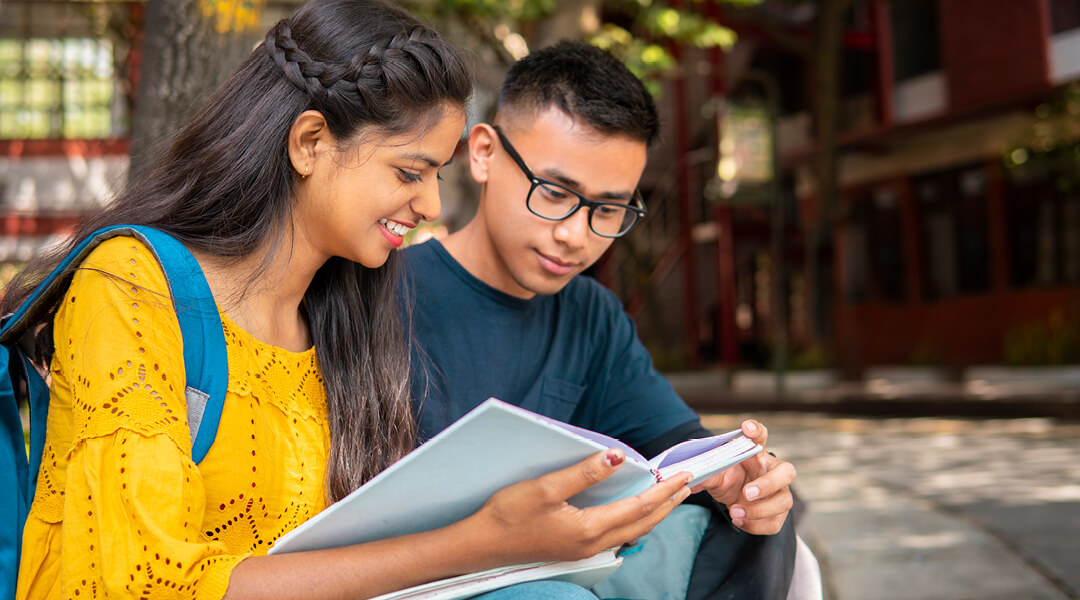 Two teenagers smiling and reading a book together.