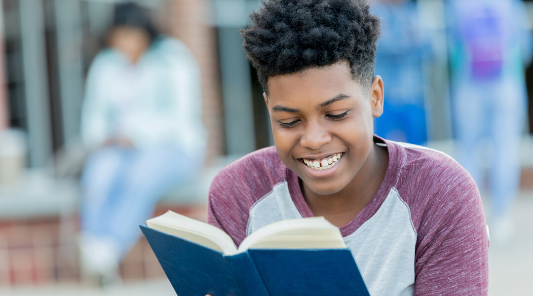Teenager smiling while reading a book.