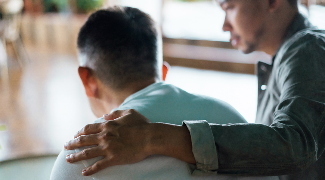 Rear view of an adult child and elderly parent sitting together at home.