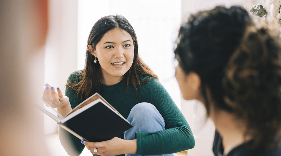 A young adult holding a book and talking with friends in book club.