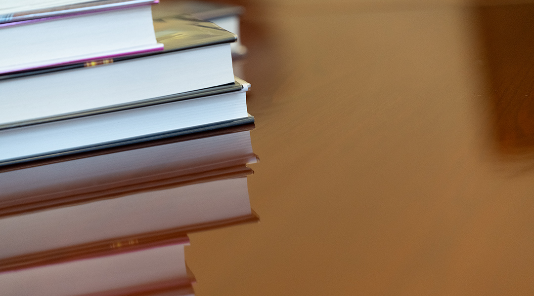 Close view of three books stacked together and their reflection on the surface of the table.