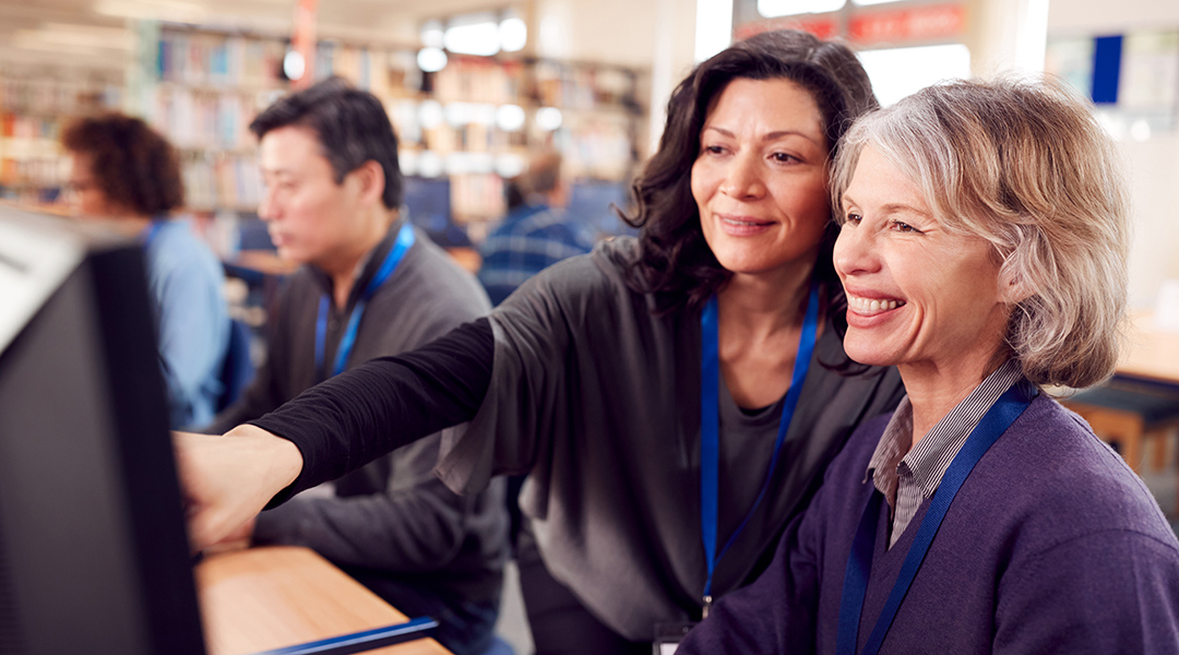 A librarian assists a mature adult on the computer.