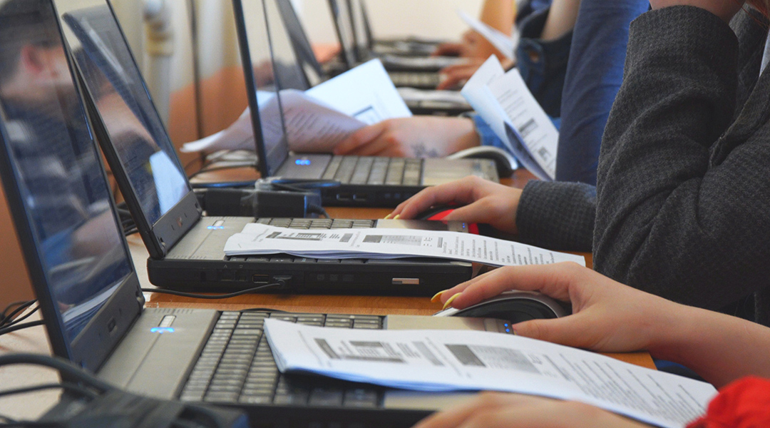 Close-up of adults in a computer class with open laptops and an instructional hand-out.