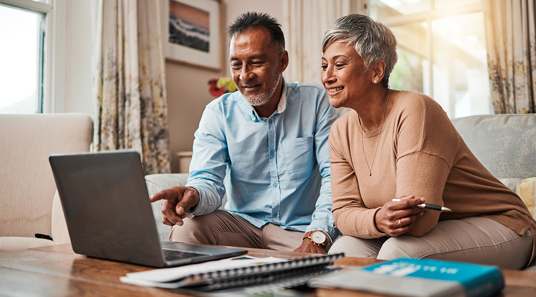 A mature couple sits together on a sofa sharing a laptop as they plan finances, retirement funding and investment or asset management at home.