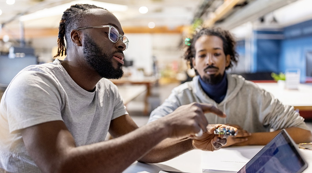 Two electrical engineers examine a microchip and its specifications.