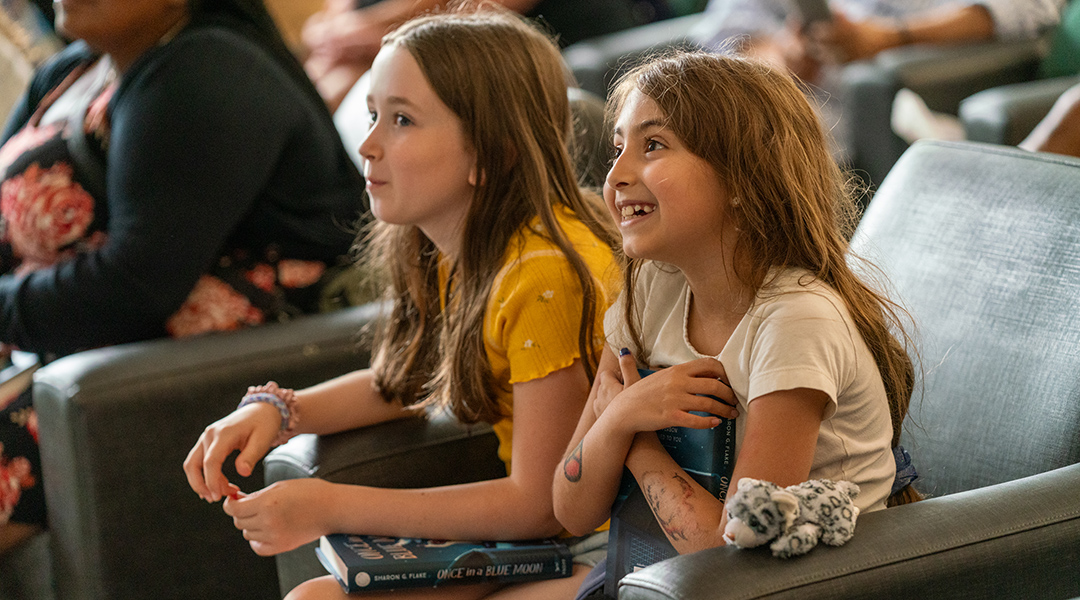 Two elementary school children excitedly watch an author presentation at the library.
