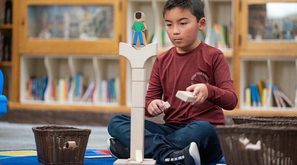 A child, about six, builds with blocks on the floor of the children's section of the library.