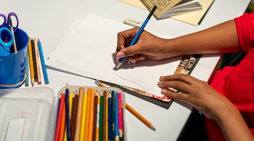 Overhead shot of a child sketching on a blank piece of paper.