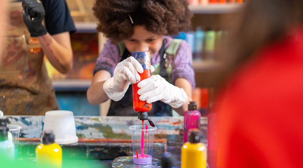 School children pour acrylic paint into a cup for a pottery project.