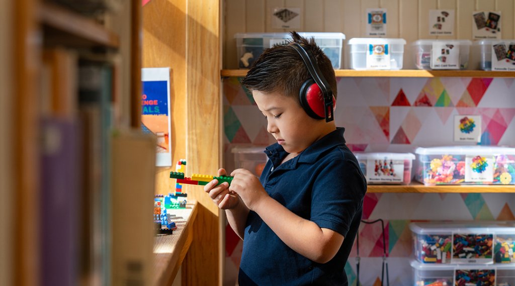 A child, about five, wears sensory headphones while playing with Legos.