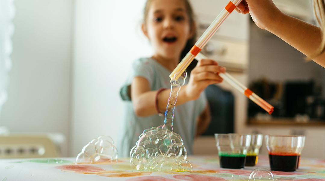 Children make watercolor art using colored liquid and bubbles on paper.