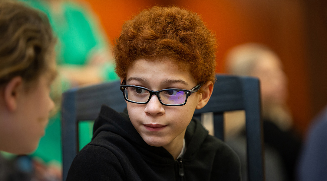 A child in glasses looks to a friend for an answer during a trivia game at the library.