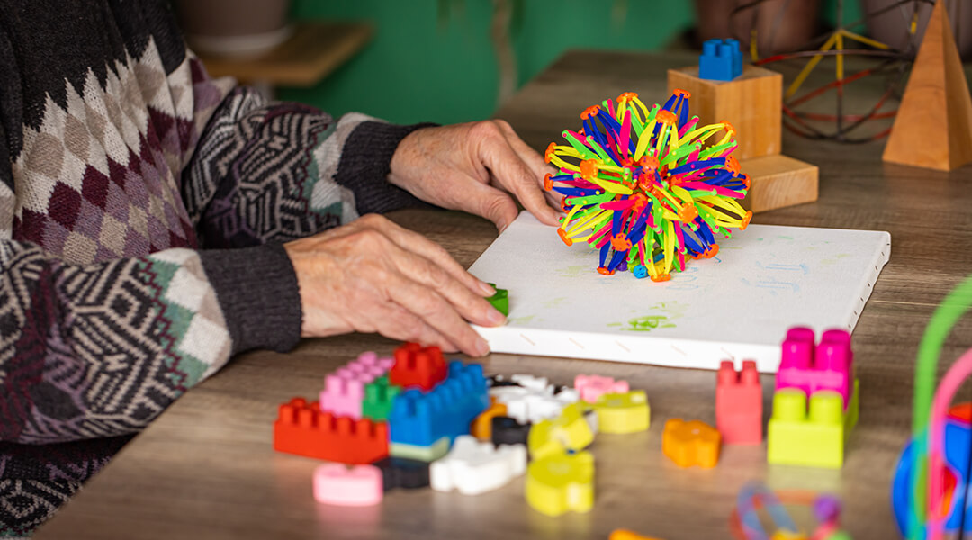 Senior adult is sitting at a table and uses colorful sensory ball.