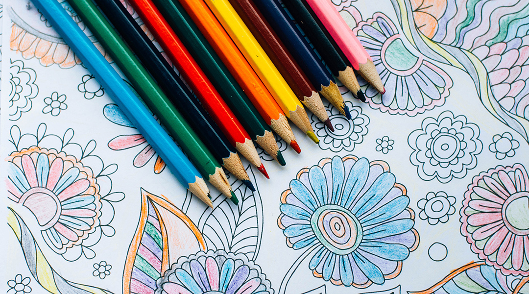 An array of colored pencils lined up on top of a coloring sheet.