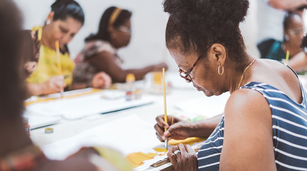 A group of adults paint a craft at a shared table.