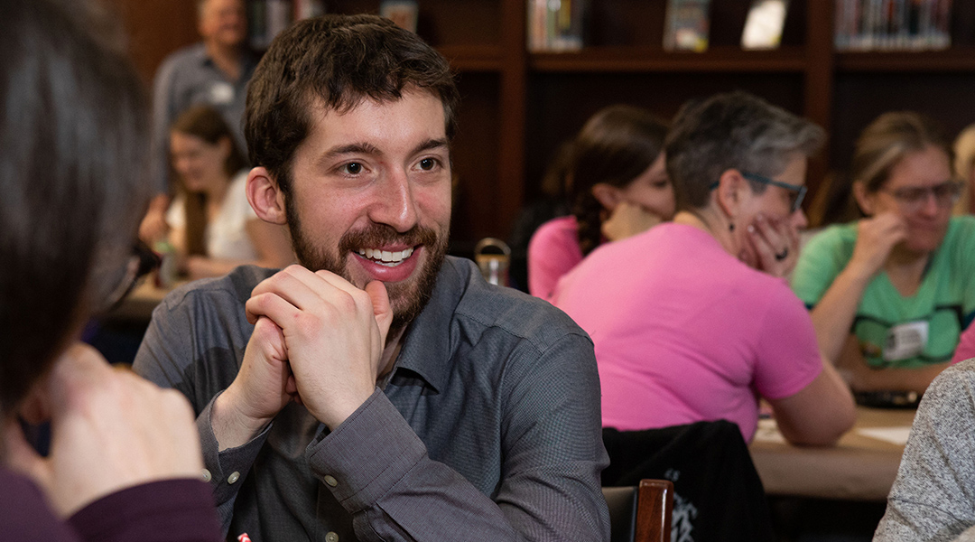 Close-up of a smiling person at a crowded table during a library event.