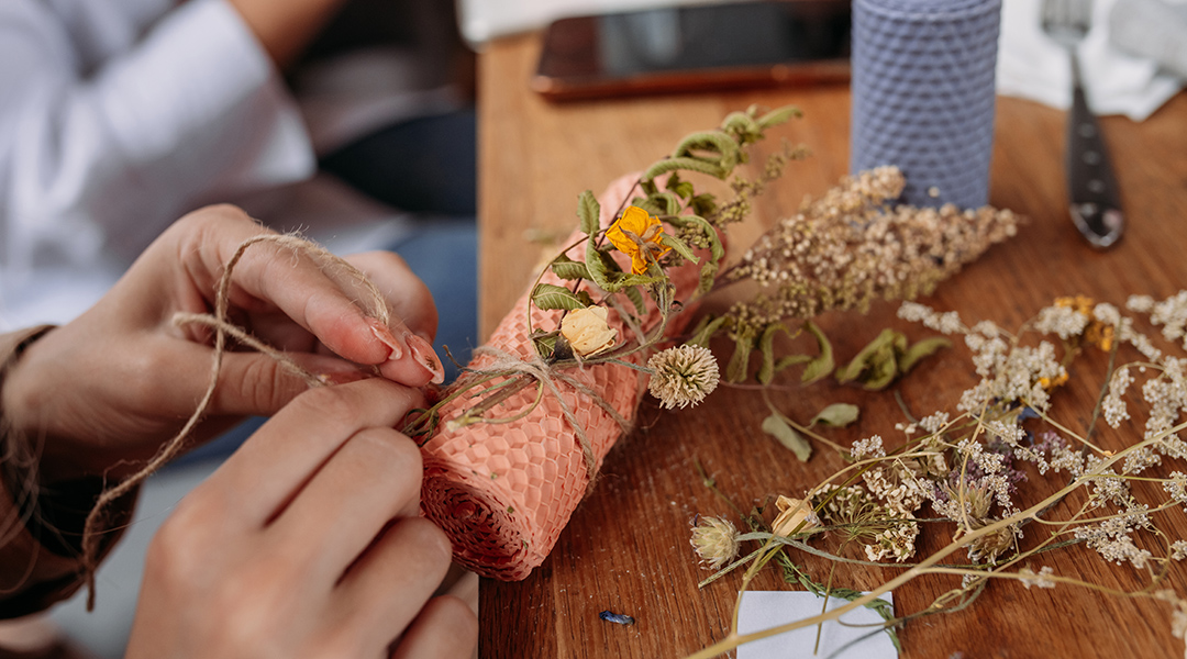 Close-up of hands as a person making a decorative wax candle decorates with dried flowers.
