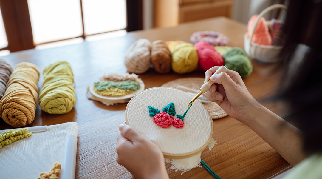 An adult uses a punch kit to make yarn flowers on cream fabric in an embroidery hoop.