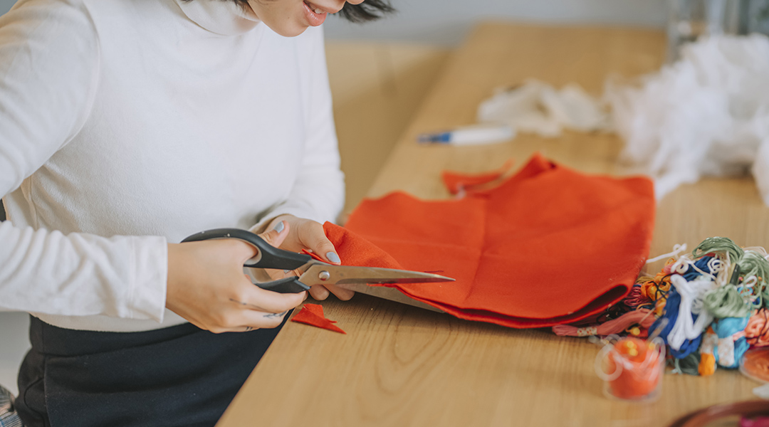 A person cutting fabric with scissors preparing for cross-stitch embroidery.