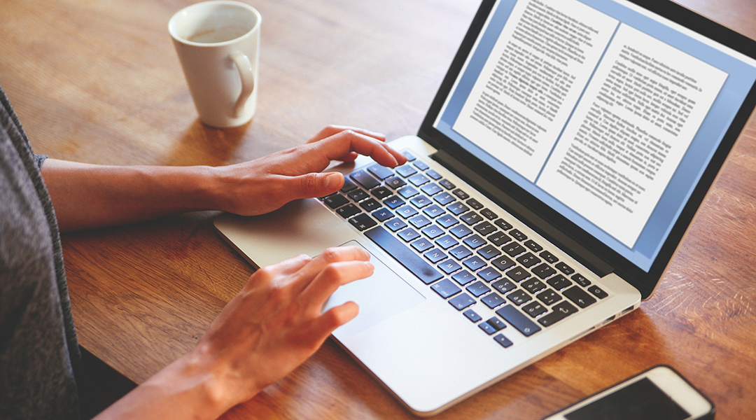 High angle image of a person typing on the laptop keyboard while having a cup of coffee.