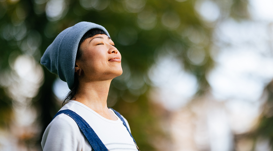 Close up photo of happy adult with closed eyes practicing deep breathing outdoors.