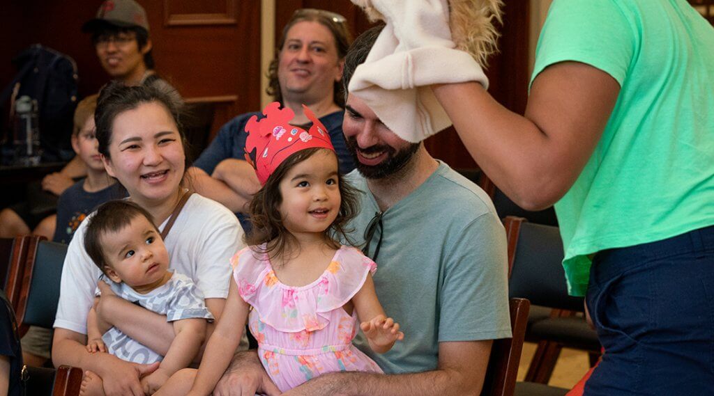 Caregivers hold young children on their laps during a puppet show.