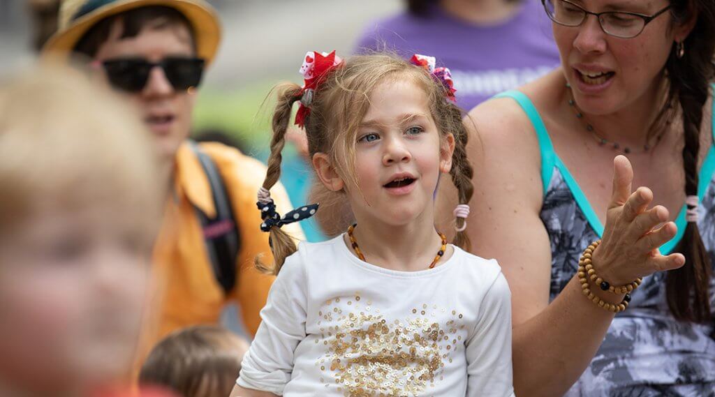 A delighted preschooler watches a presentation with other children and caregivers.