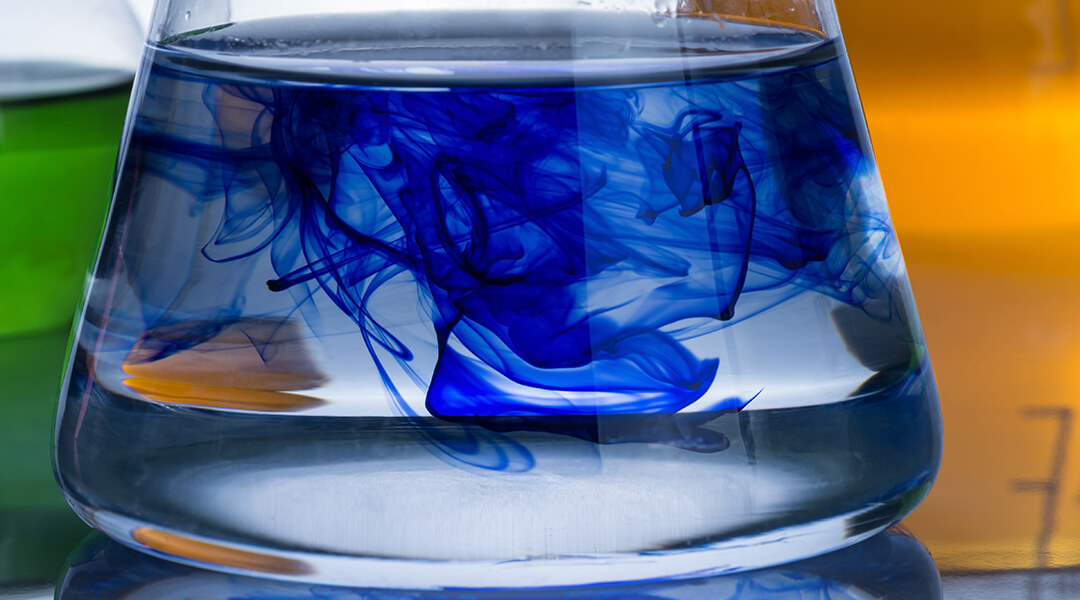 Close-up of the liquid in a chemistry beaker, blue color diffusing into clear water.