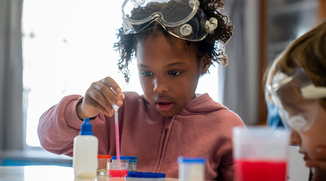 A young child looks very focused during science class while they mix liquids.