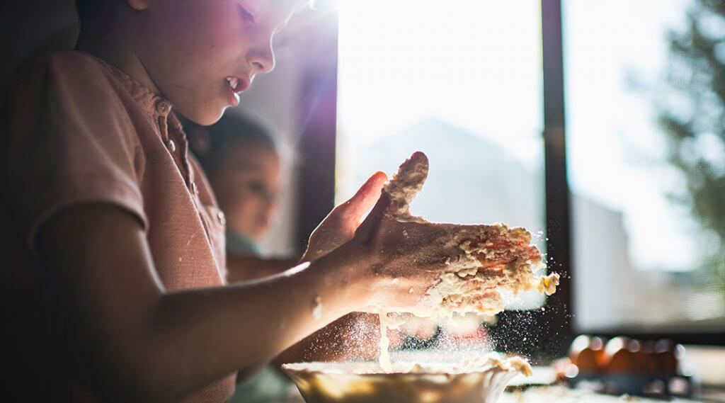 Two young children prepare dough in the kitchen, hands covered in flour.